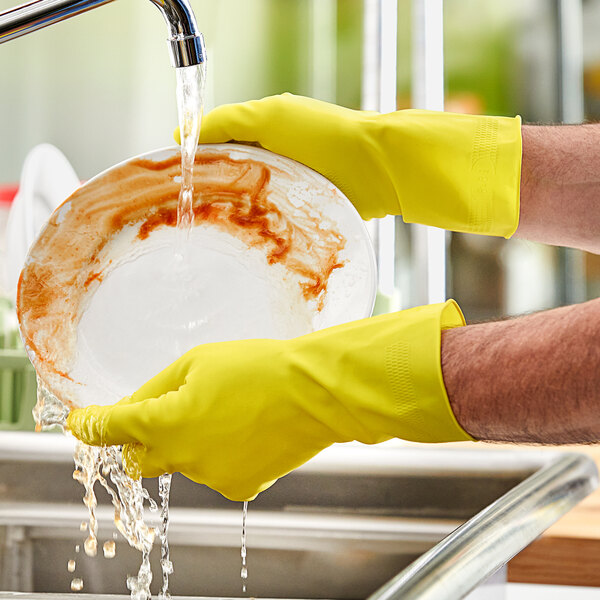 A person wearing Lavex yellow latex gloves washing a plate.