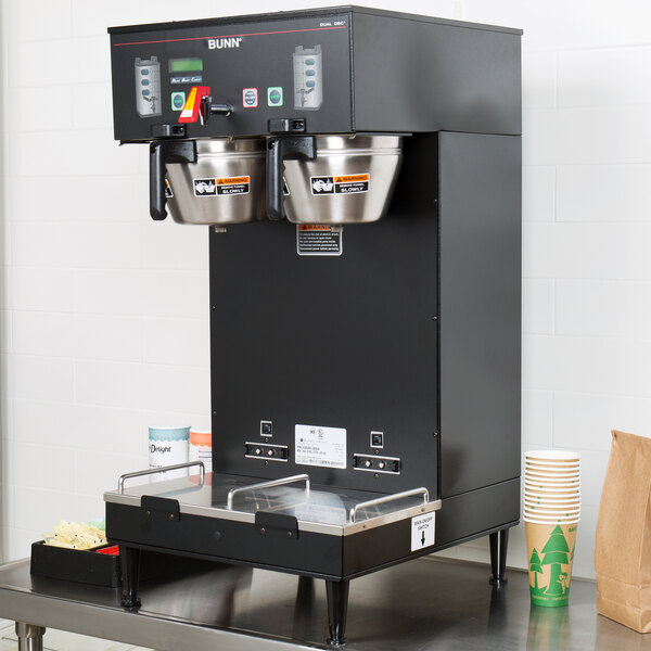 A Bunn BrewWISE commercial coffee maker on a counter with two cups on it.