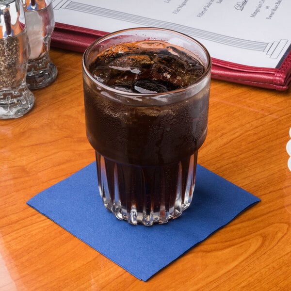 A glass of soda with ice on a navy blue Hoffmaster beverage napkin.