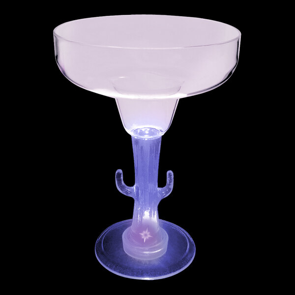 A clear plastic margarita glass with a cactus shaped stem and a purple LED light on the table.