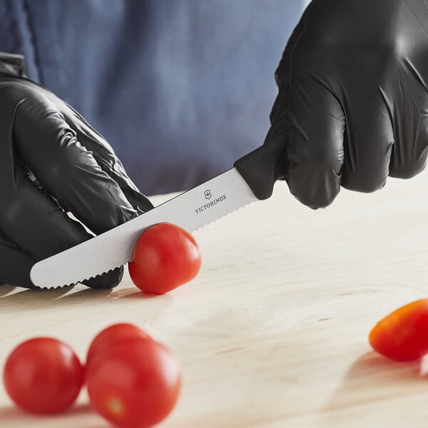 A gloved hand uses a Victorinox utility knife to cut a tomato.