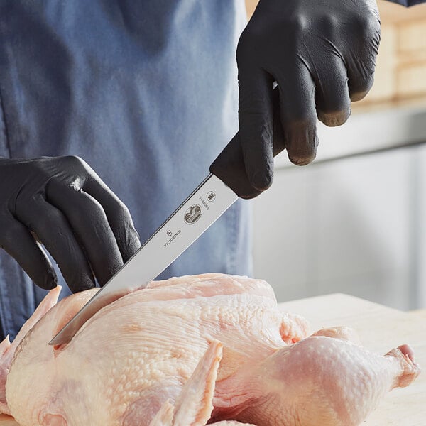 A person wearing black gloves uses a Victorinox extra-wide boning knife to cut a chicken.