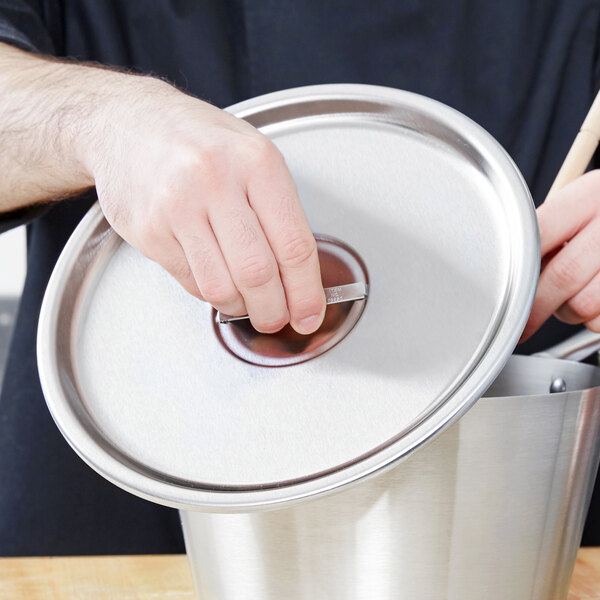 A person holding a Vollrath stainless steel lid over a pot.