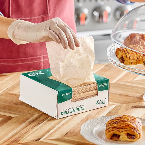 A person in gloves using EcoChoice Natural Kraft Deli Wrap to pick up pastries from a bakery display.