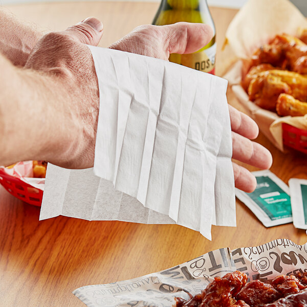 A hand using a Choice lemon scented moist towelette to clean hands over a table with chicken wings.