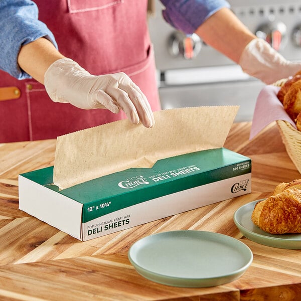 A person wearing gloves and using EcoChoice interfolded natural kraft wax paper to wrap a croissant.