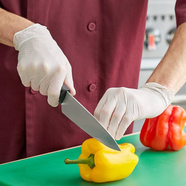 A person in a white coat cutting a yellow bell pepper on a counter with Noble Products Powder-Free Disposable Latex Gloves.