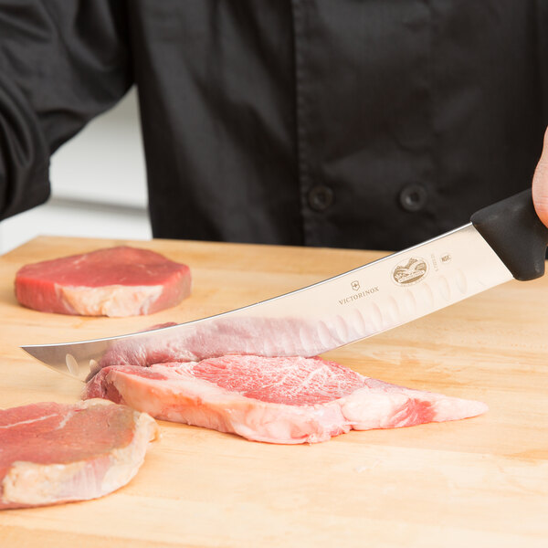 A Victorinox cimeter knife with a black handle cutting meat on a cutting board.