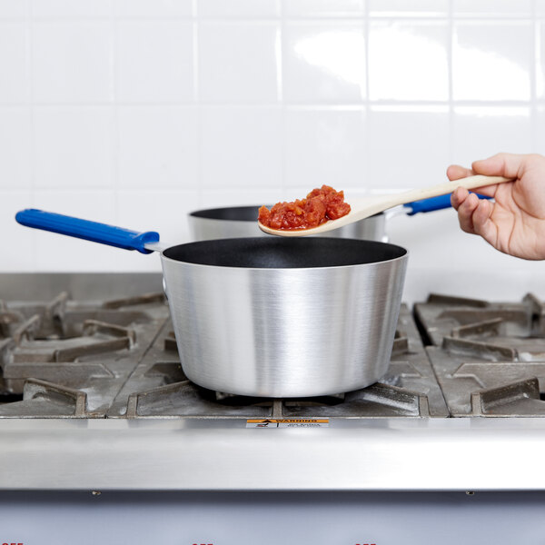 A person stirring food in a Vollrath Wear-Ever sauce pan.