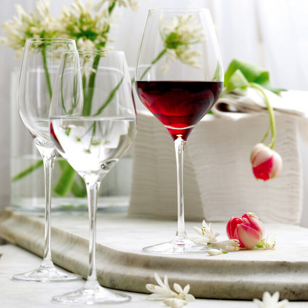 Three Stolzle Exquisit Royal white wine glasses on a marble table with a glass of red wine.