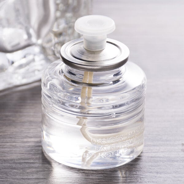 A close-up of a Sterno clear liquid wax cartridge in a small glass bottle with a lid.