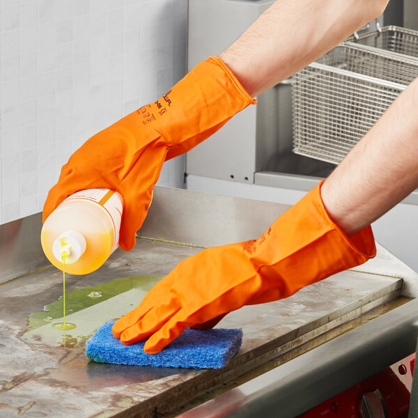 A person wearing orange Showa biodegradable nitrile gloves pouring liquid onto a surface.