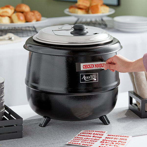 A hand opening a large black Avantco soup kettle.