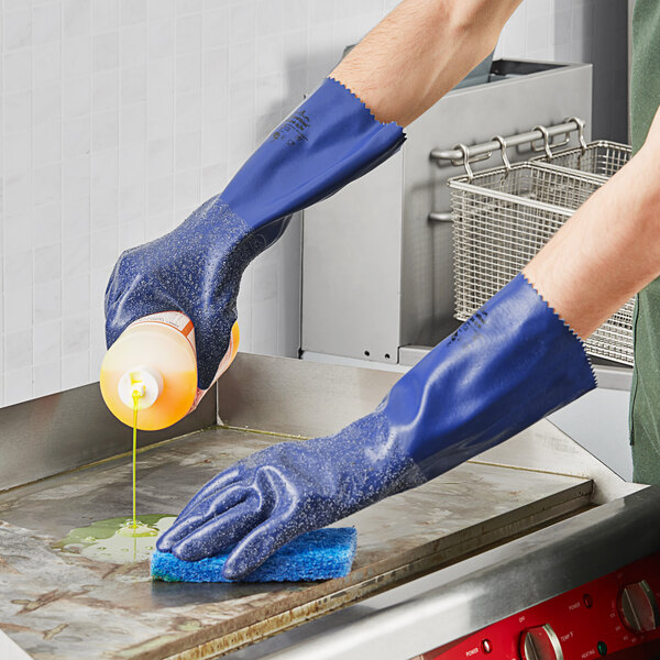 A person wearing blue Showa gloves cleaning a surface.