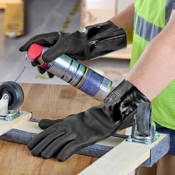 A person wearing black Showa neoprene gloves using a spray can.