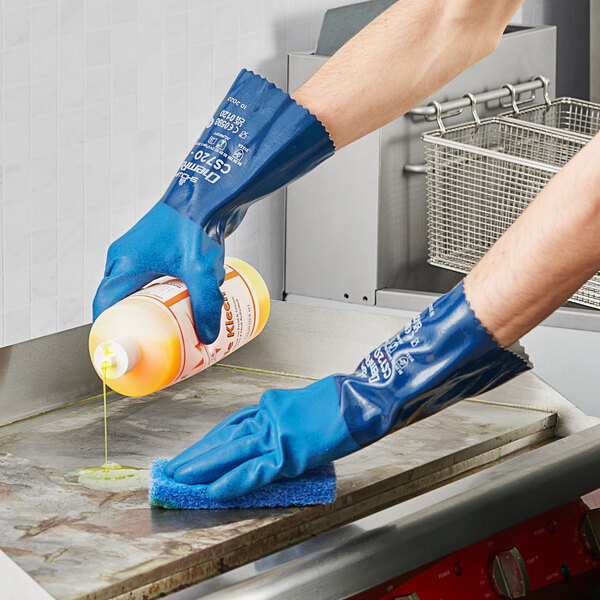 A person wearing a blue Showa dishwashing glove cleaning a counter.