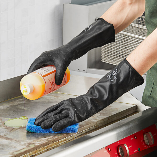 A person wearing Showa black neoprene gloves pouring cleaning liquid onto a counter.