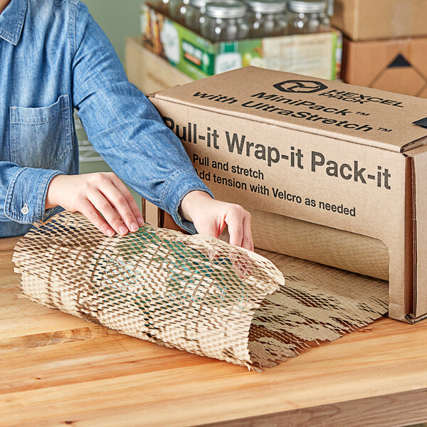 A person using a HexcelWrap MiniPack dispenser box to pack a brown box.