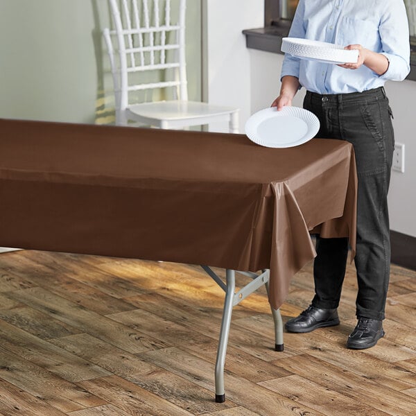 A woman holding a plate over a table with a Choice chocolate plastic table cover.