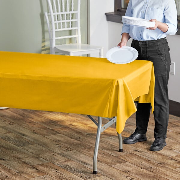 A hand holding a yellow plastic table cover over a table with a white plate.