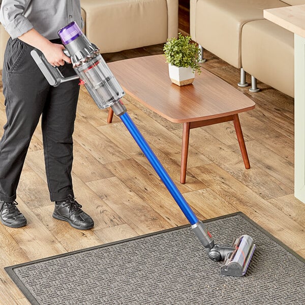 A woman using a Dyson V11 cordless stick vacuum to clean a white rug.
