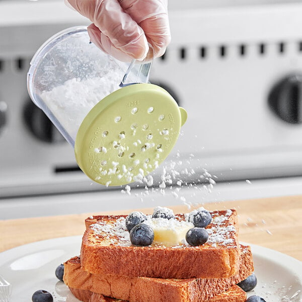 A gloved hand with a yellow Carlisle shaker pouring powder onto french toast.