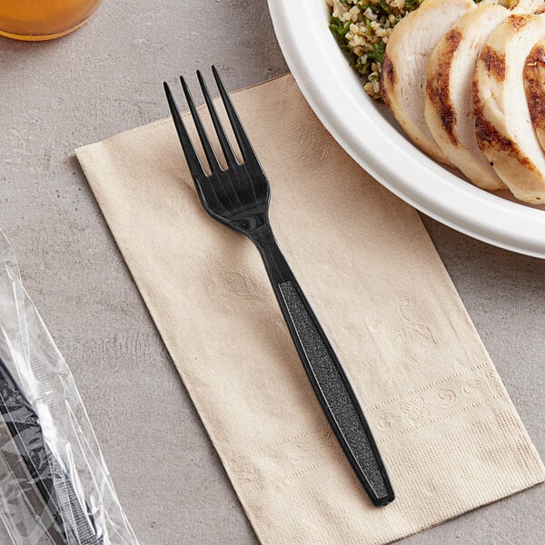 A black plastic Visions heavy weight fork on a napkin next to a bowl of food.