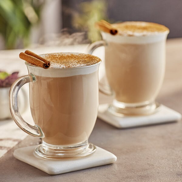 A glass mug of Capora Original Chai Tea Latte with cinnamon sticks.
