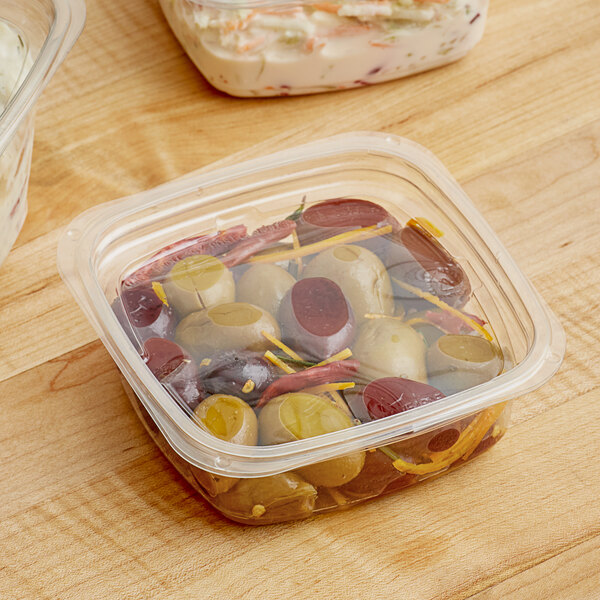 A Pactiv plastic deli container filled with food on a wooden table.