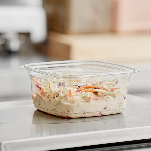A Pactiv plastic deli container filled with coleslaw on a counter.