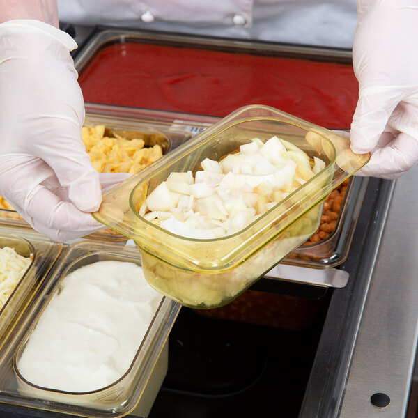 A person in white gloves using a Cambro amber plastic food pan to serve food.