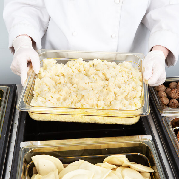 A person in a white uniform holding a Cambro amber plastic food pan of mashed potatoes.