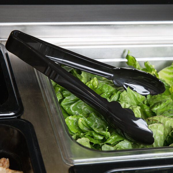 Black Carlisle plastic utility tongs serving salad in a container on a salad bar counter.