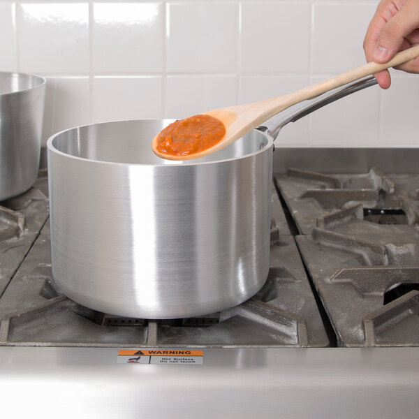 A person using a Vollrath Wear-Ever sauce pan to stir food on a stove.