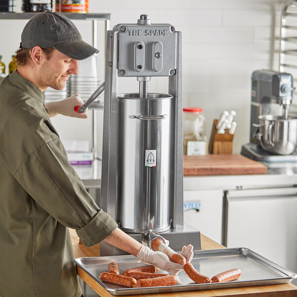 A man using a Tre Spade stainless steel vertical sausage stuffer on a counter in a butcher shop.