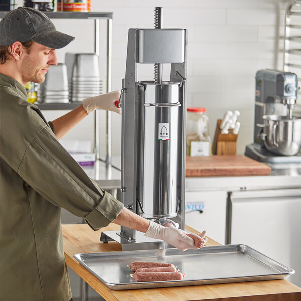 A man wearing gloves uses a Tre Spade stainless steel sausage stuffer on a countertop.
