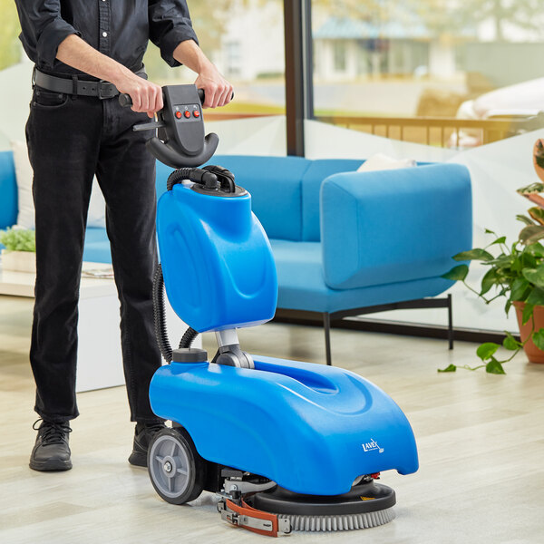 A person using a Lavex cordless walk behind floor scrubber to clean a floor.