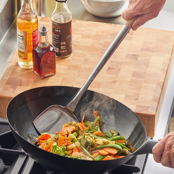 An Emperor's Select large wok spatula stirring food in a wok.