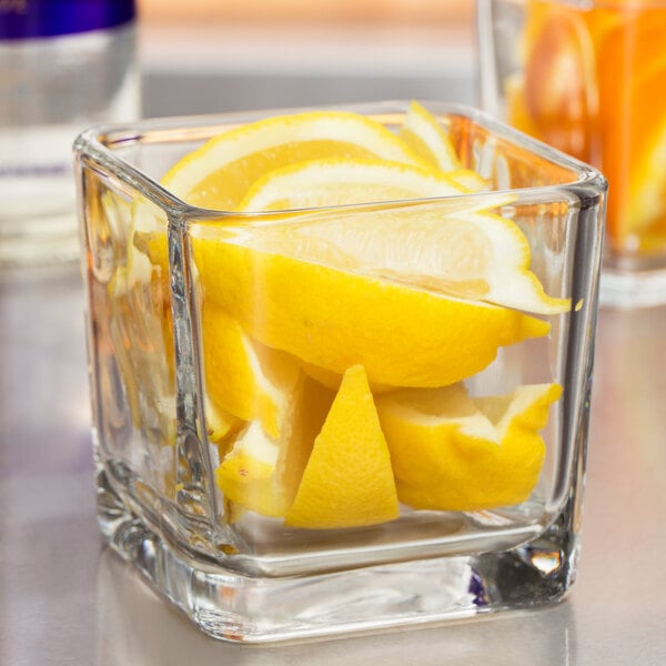 A Libbey cube votive holder with lemon slices in it.