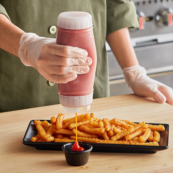 A person using a San Jamar sauce bottle to pour sauce on fries.