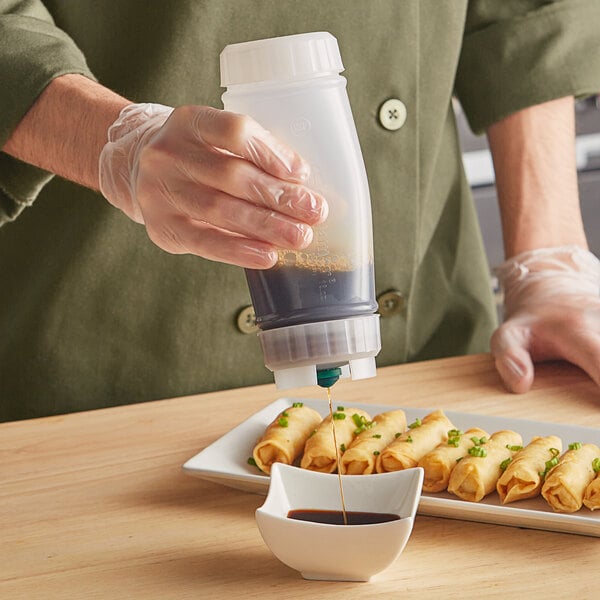 A hand holding a San Jamar sauce bottle pouring sauce onto a bowl of food.