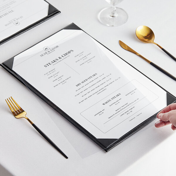A menu with a clear plastic cover and a fork and spoon with gold handles.