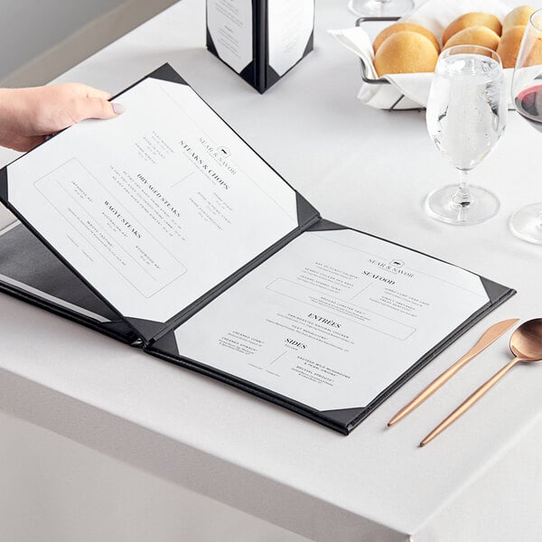 A hand holding an Acopa Prime black vinyl menu on a table.