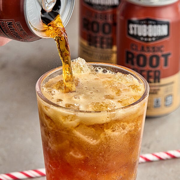 A person pouring Stubborn Classic Root Beer from a can into a glass with a straw.