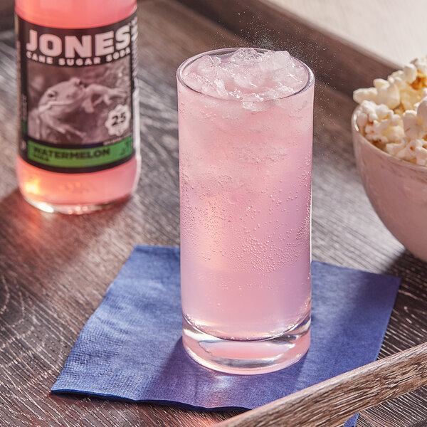 A glass of Jones Watermelon Soda with ice next to a bowl of popcorn.