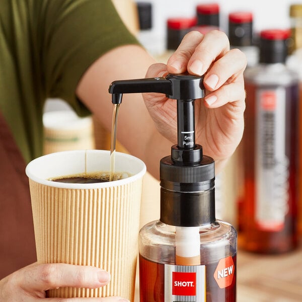 A person using a SHOTT syrup pump to pour coffee into a cup.