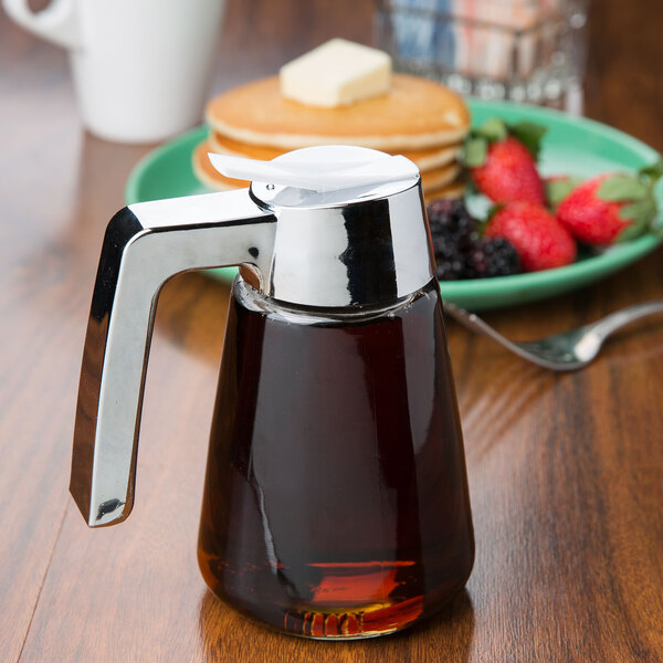 A Tablecraft glass syrup dispenser with a chrome top on a table with pancakes and berries.