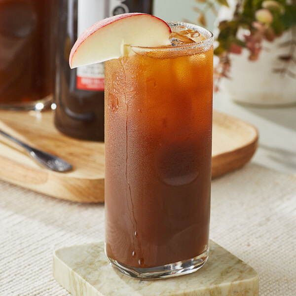 A glass of SHOTT Black Tea and Peach Concentrate with ice, liquid, and a slice of apple.