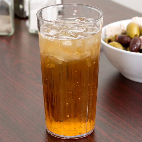 A Carlisle clear plastic tumbler filled with iced tea on a table.
