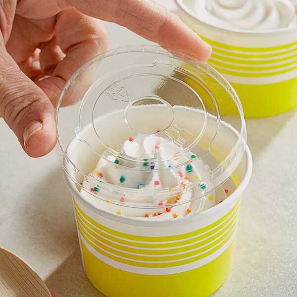 A hand holding a Choice plastic container of frozen yogurt with white frosting and sprinkles.